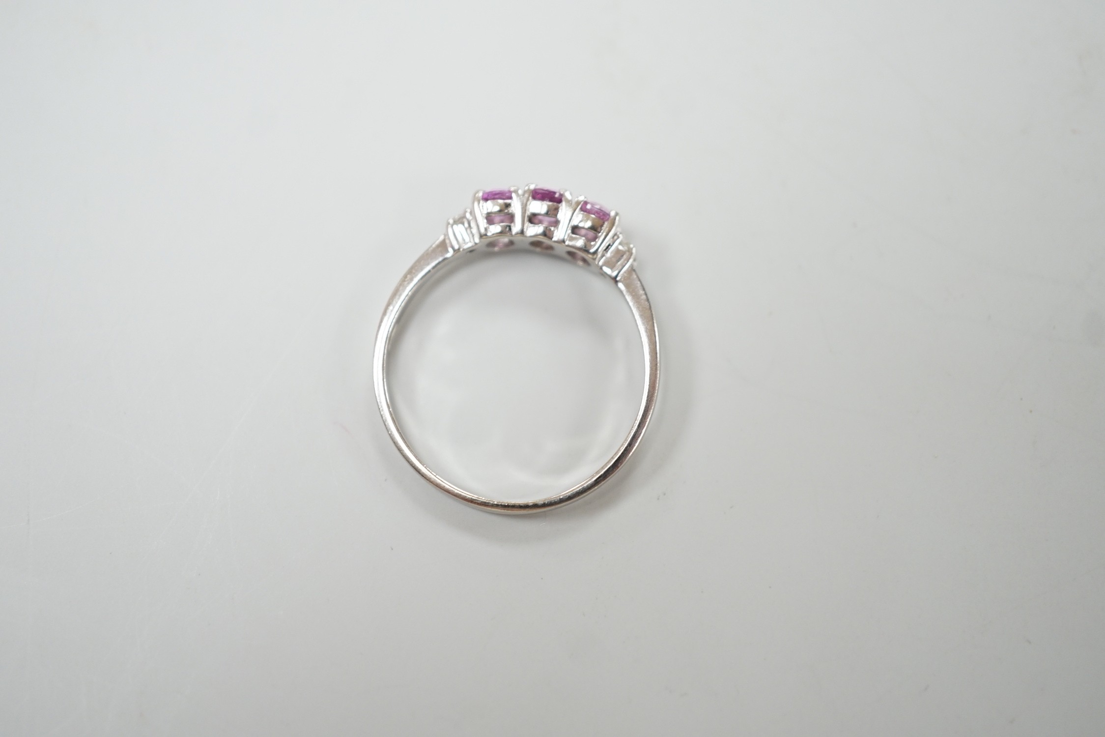 A modern 14ct white gold, three stone pink sapphire and two stone diamond chip set ring, size L, gross weight 1.5 grams.